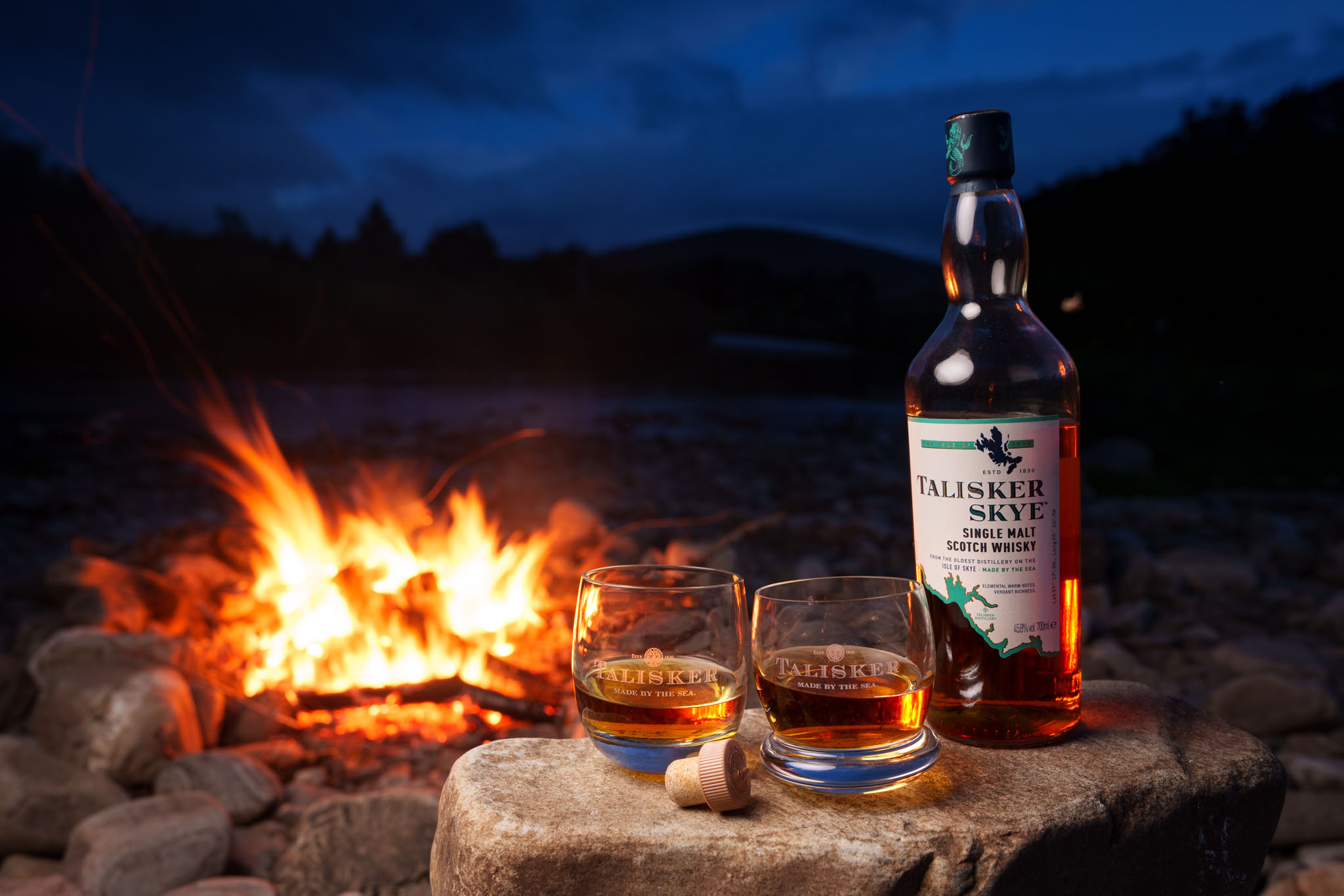 Whisky glass lit by open fire riverside Scotland – on location product photography