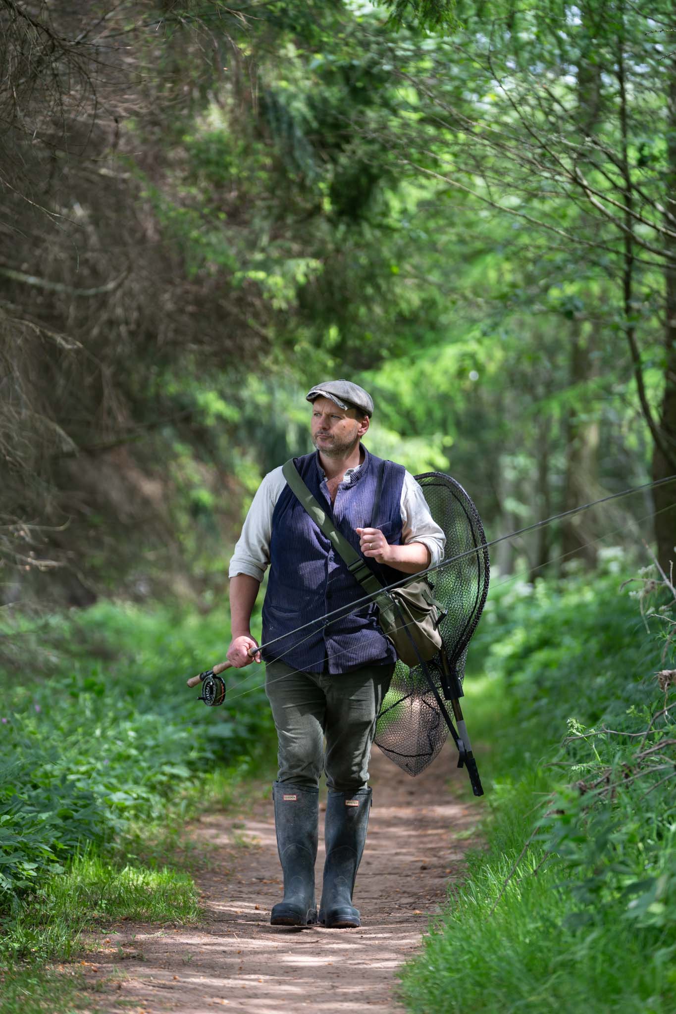 Tom Godber-Ford Moore walking a riverside path carrying a fly rod and landing net by fishing photographer Scotland