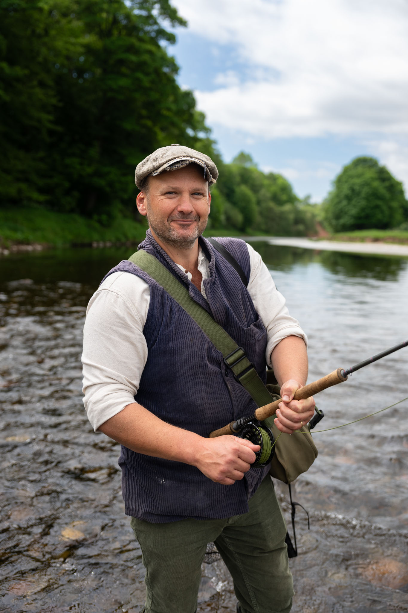 Portrait of Tom Godber-Ford Moore holding a fly rod on the riverbank