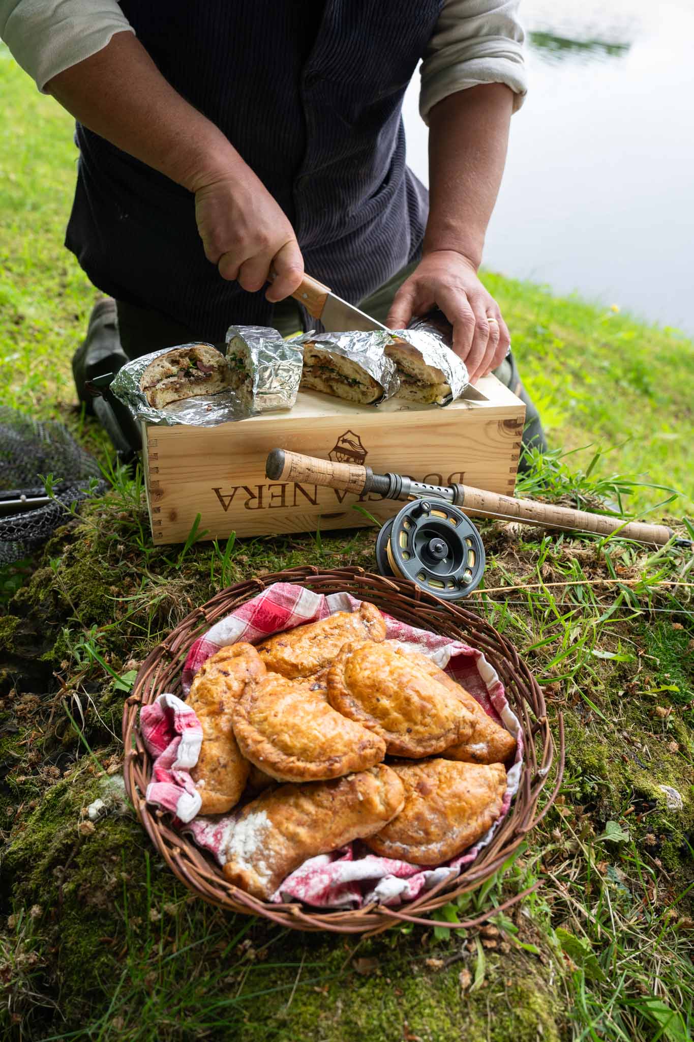Slicing a foil-wrapped pheasant pissaladière pan bagnat on a wooden board by the river
