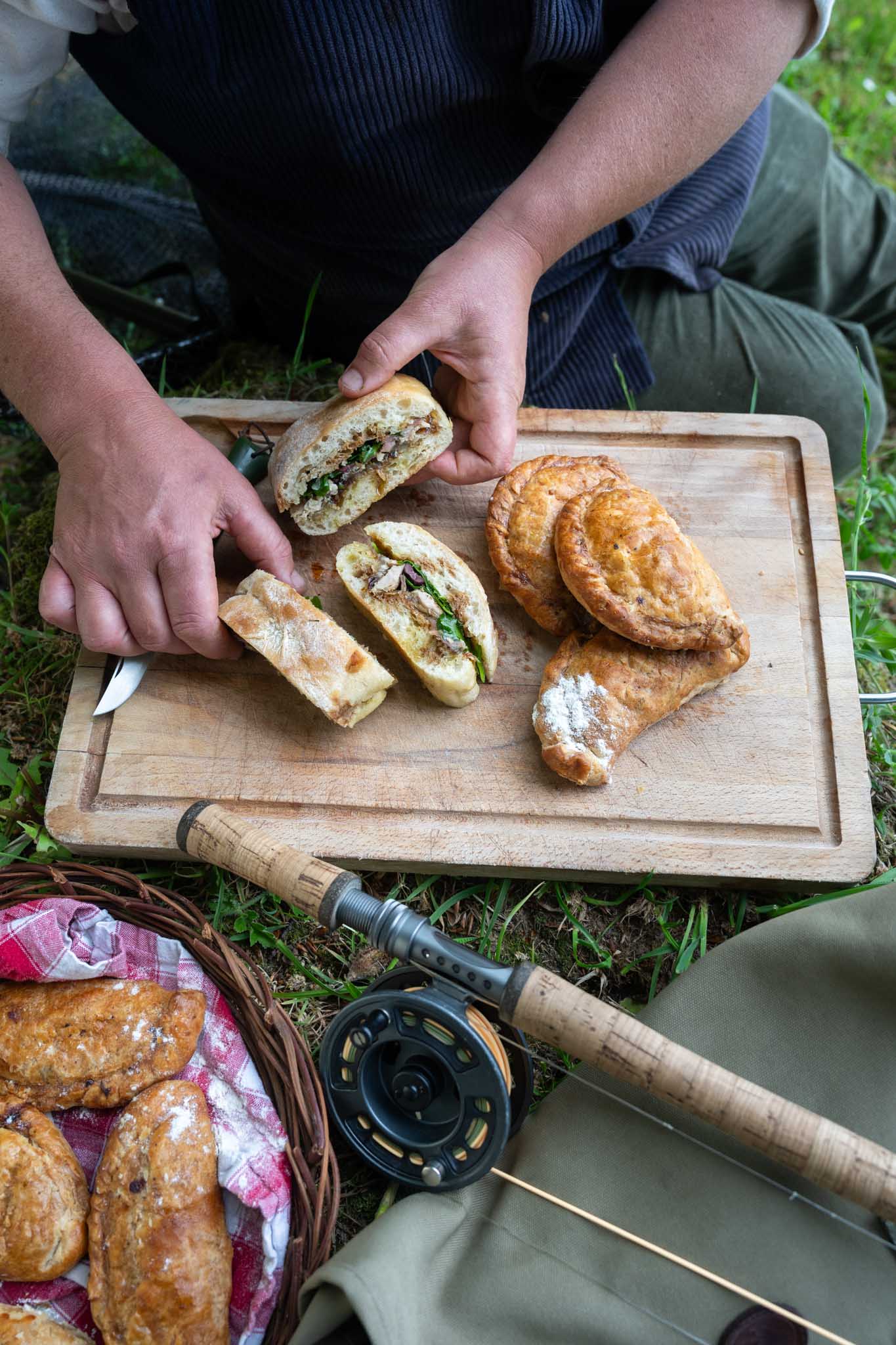 Overhead shot of hands serving venison pasties and pan bagnat on a picnic board
